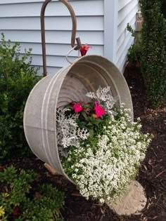 a metal bucket with flowers in it sitting on the side of a house next to some bushes