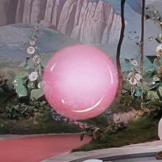 a pink ball floating in the air next to a wall with mountains and flowers on it