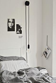 a bedroom with white walls and grey linens on the bed, along with black and white photos