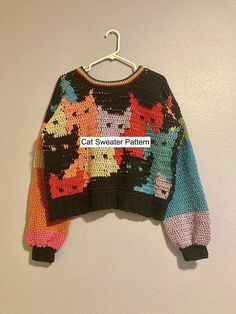 a multicolored sweater hanging on a white wall next to a black hanger