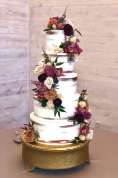 a three tiered wedding cake with purple and white flowers on the top, sitting on a gold platter