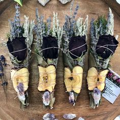 four dried flowers are wrapped in twine and placed on a wooden platter with rocks