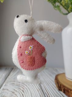 a white stuffed animal hanging from a string on a wooden table next to a potted plant