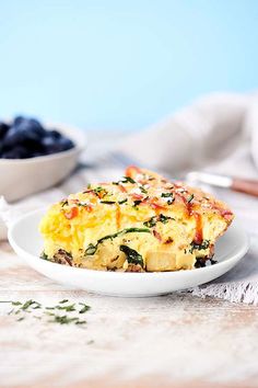 a white plate topped with an omelet next to a bowl of blueberries