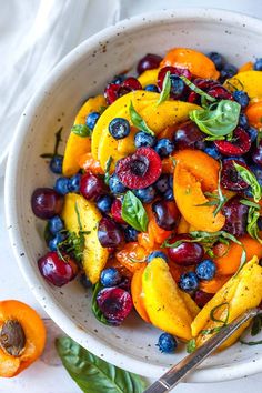 a white bowl filled with fresh fruit and herbs on top of a table next to an orange slice