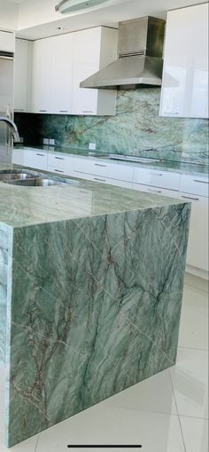 a kitchen with marble counter tops and white cabinets in the background is an island sink