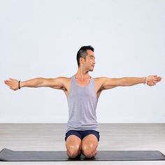 a man sitting on a yoga mat with his arms stretched out