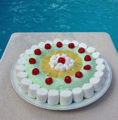 a cake with marshmallows, pineapple and cherries on it next to a swimming pool