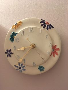 a white clock with flowers painted on it's face and hands, hanging from the wall