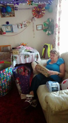 a woman sitting on a couch in a room with christmas decorations and presents around her