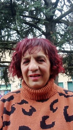 a woman with red hair is wearing an orange sweater and smiling at the camera while standing in front of a tree