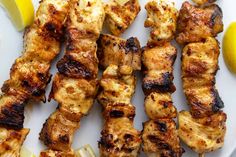 chicken skewers with lemon wedges on a white plate