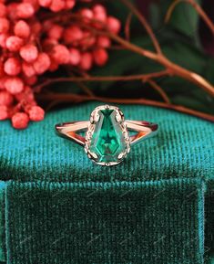 an emerald colored ring sitting on top of a green velvet covered box next to red berries