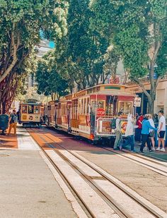 people are standing on the sidewalk next to a trolley car that is going down the street