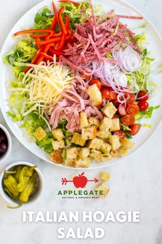 a salad with meat, cheese and vegetables in it on a white plate next to two small bowls