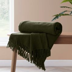 a green blanket sitting on top of a wooden bench next to a potted plant