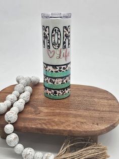 the mom life tumbler is sitting on top of a wooden table next to some beads