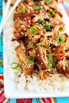 a white plate topped with rice covered in meat and veggies next to chopsticks