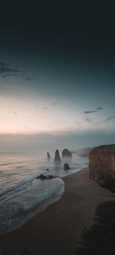 the beach is empty and has waves coming in from the ocean at dusk, with two large rocks sticking out of the water