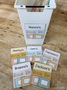 three book bins with books in them sitting on a wooden floor next to a trash can