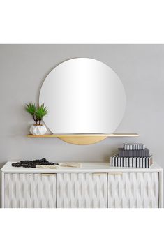 an oval mirror on the wall above a white cabinet with books and a potted plant