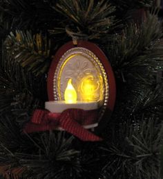 an ornament hanging from a christmas tree decorated with lights and bows, in the shape of a candle