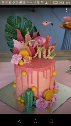 a pink cake with flamingos and flowers on top is decorated with the word one