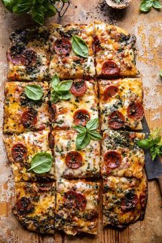 a pizza cut into squares on top of a wooden cutting board with basil and pepperoni