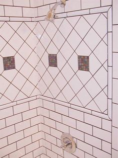 a white tiled shower with three square holes in the wall