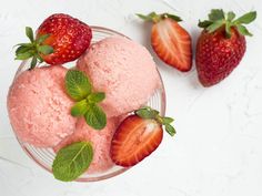 two scoops of ice cream and three strawberries on a white surface with green leaves