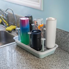 there is a tray with cups and bottles on the kitchen sink counter next to the faucet