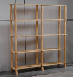 a wooden book shelf sitting on top of a floor next to a gray wall and white carpet