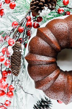 a bundt cake sitting on top of a white plate next to pine cones and berries