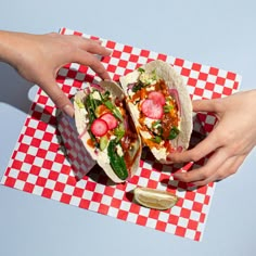 two hands reaching for some tacos on a checkered table cloth