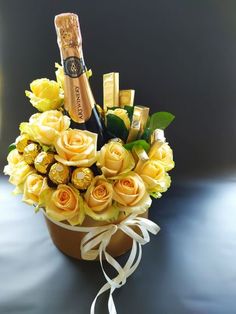 a bouquet of yellow roses and champagne bottles in a brown vase on a black surface