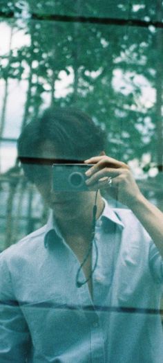 a man taking a selfie in front of a glass window with trees behind him