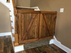 a wooden gate in the corner of a room with hardwood floors and stairs leading up to it