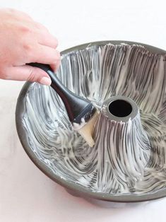 a person using a brush to paint a metal bowl with black and white swirls