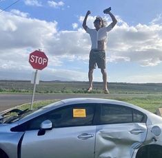 a man standing on top of a car next to a stop sign