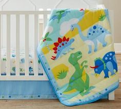 a baby crib with a blue and yellow blanket on it, next to a white crib bed