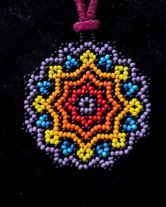 a colorful beaded ornament hanging on a black surface with a pink ribbon