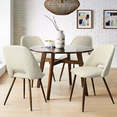 a dining table with four chairs and a vase on the top, in front of a white brick wall