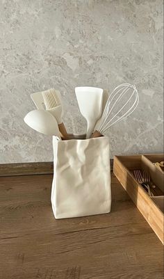 a white bag with utensils in it sitting on a wooden table next to a drawer