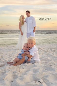 a little boy sitting on top of a sandy beach next to his mom and dad