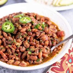 a white bowl filled with chili beans and jalapenos on top of a table