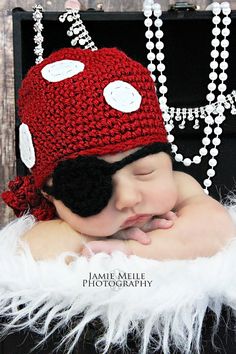 a baby wearing a red crocheted hat with white buttons on it's face