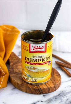 a can of pumpkin spice sitting on top of a wooden board next to cinnamon sticks