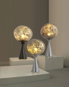 three glass globes with lights on them sitting on top of some white pedestals