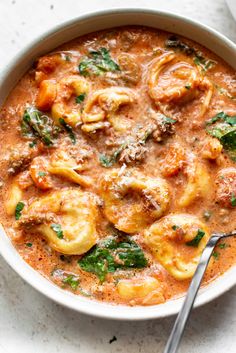 a white bowl filled with pasta and spinach in tomato sauce on top of a table