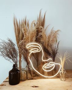 a wooden table topped with vases filled with dry grass and lights in the shape of a face